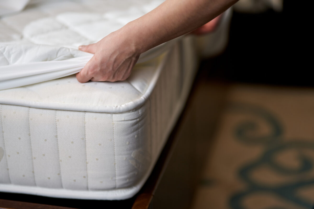 Close up of maid changing clean sheet on white mattress in hotel room while cleaning. Hotel service concept